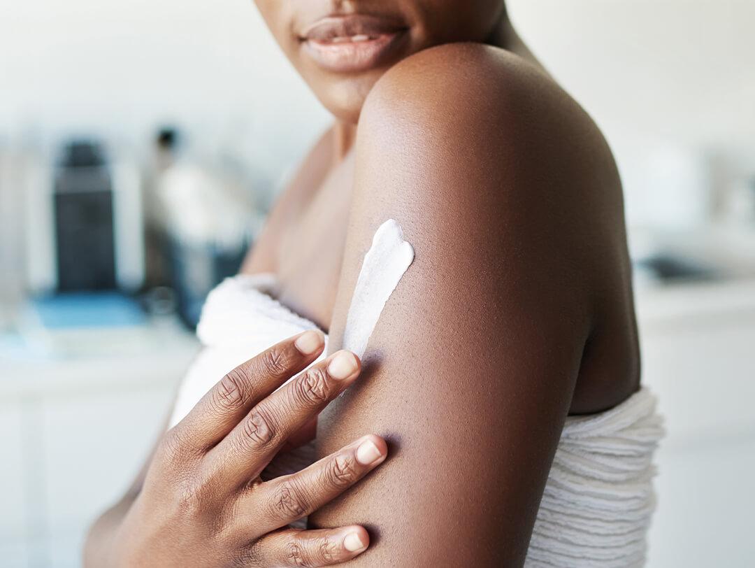 Close-up of a Black woman with a white towel wrapped around her applying cream on her arm Desktop