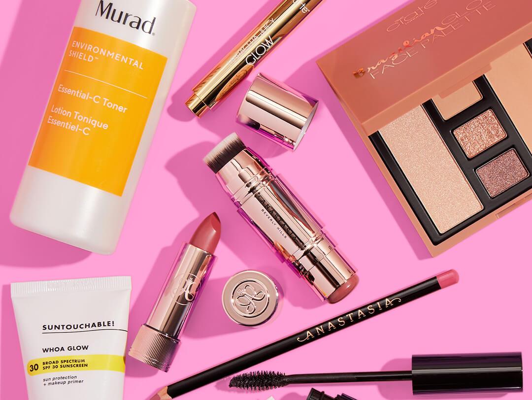 Beauty and makeup products and tools from various brands scattered on pink background Desktop