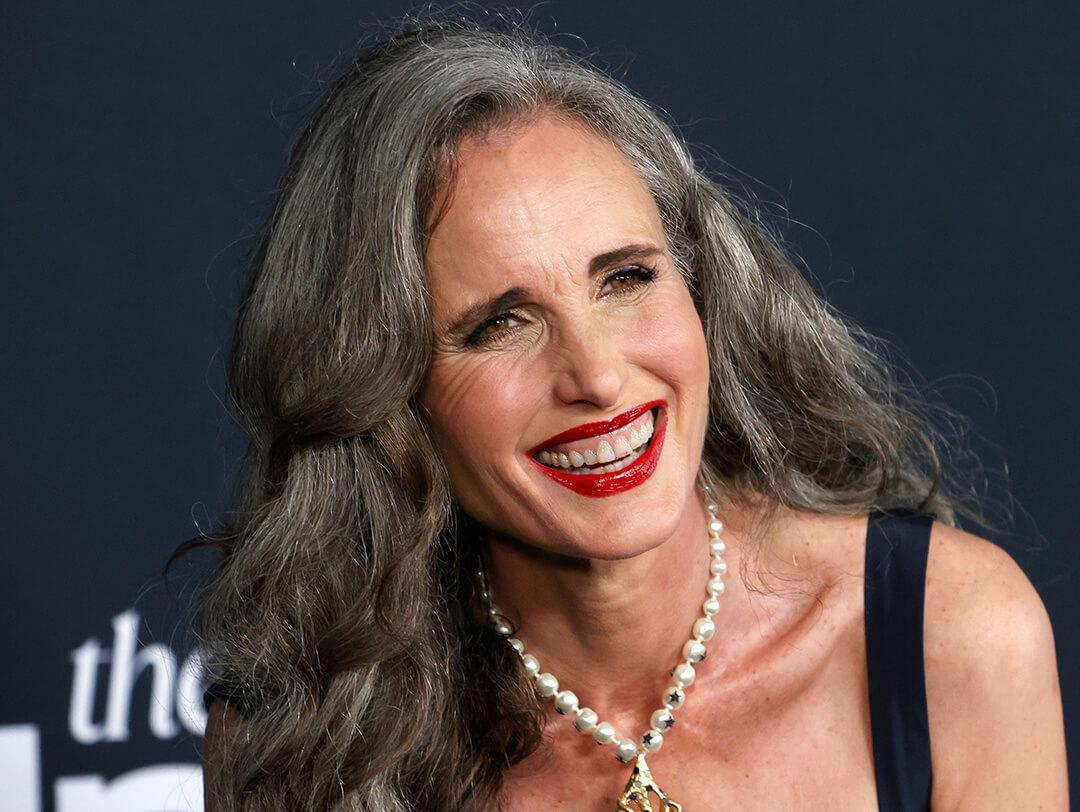 A photo of Andie MacDowell with a smokey eye makeup and red lip look wearing a black dress and a pearl necklace Desktop