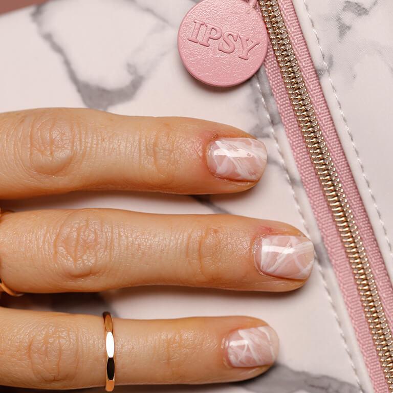 An image of three fingers with pink and white marble nail art resting on a pink and grey marble designed bag Desktop