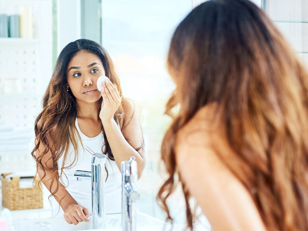 Woman removing makeup using a round cotton pad in front of a mirror Desktop