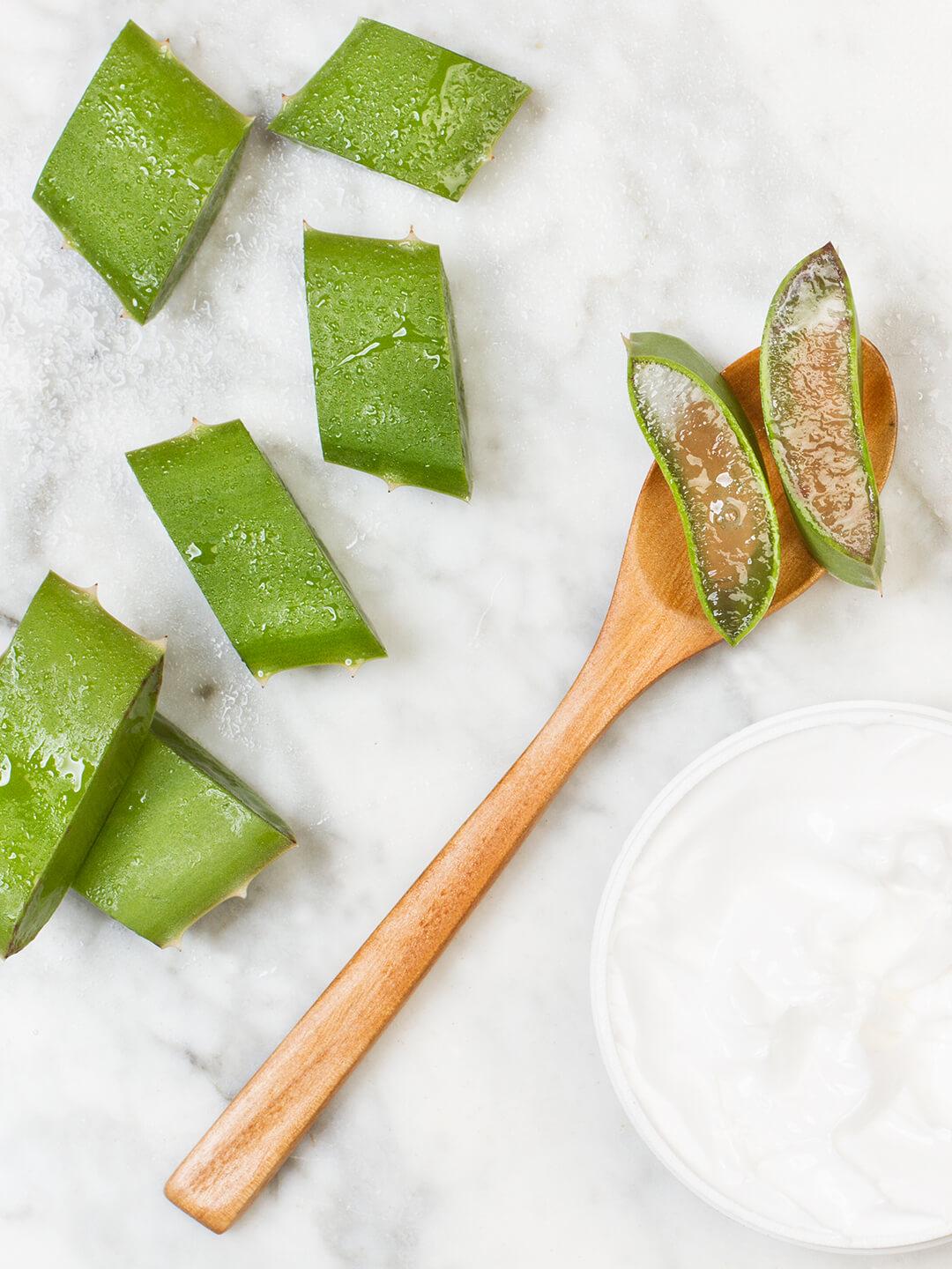 Pieces of aloe vera, wooden spoon, and a jar of cream on white, powdery sand Desktop