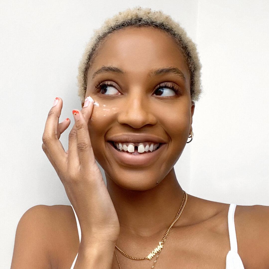 Close-up of a smiling model putting on face cream under her eyes Desktop