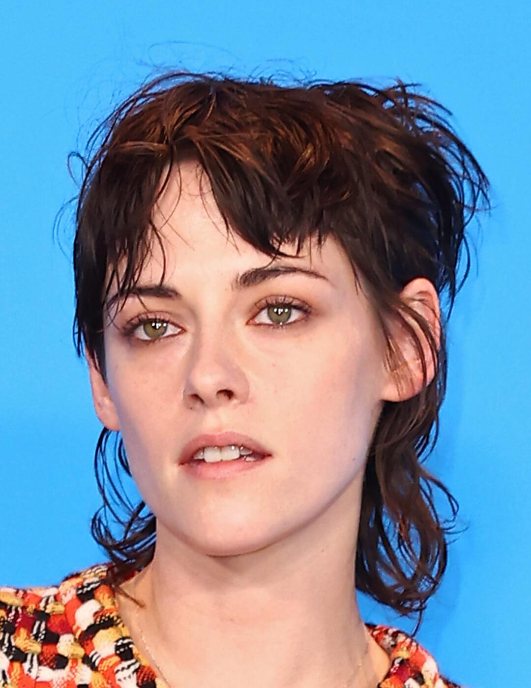 A photo of Kristen Stewart with a modern mullet with a blue background Mobile