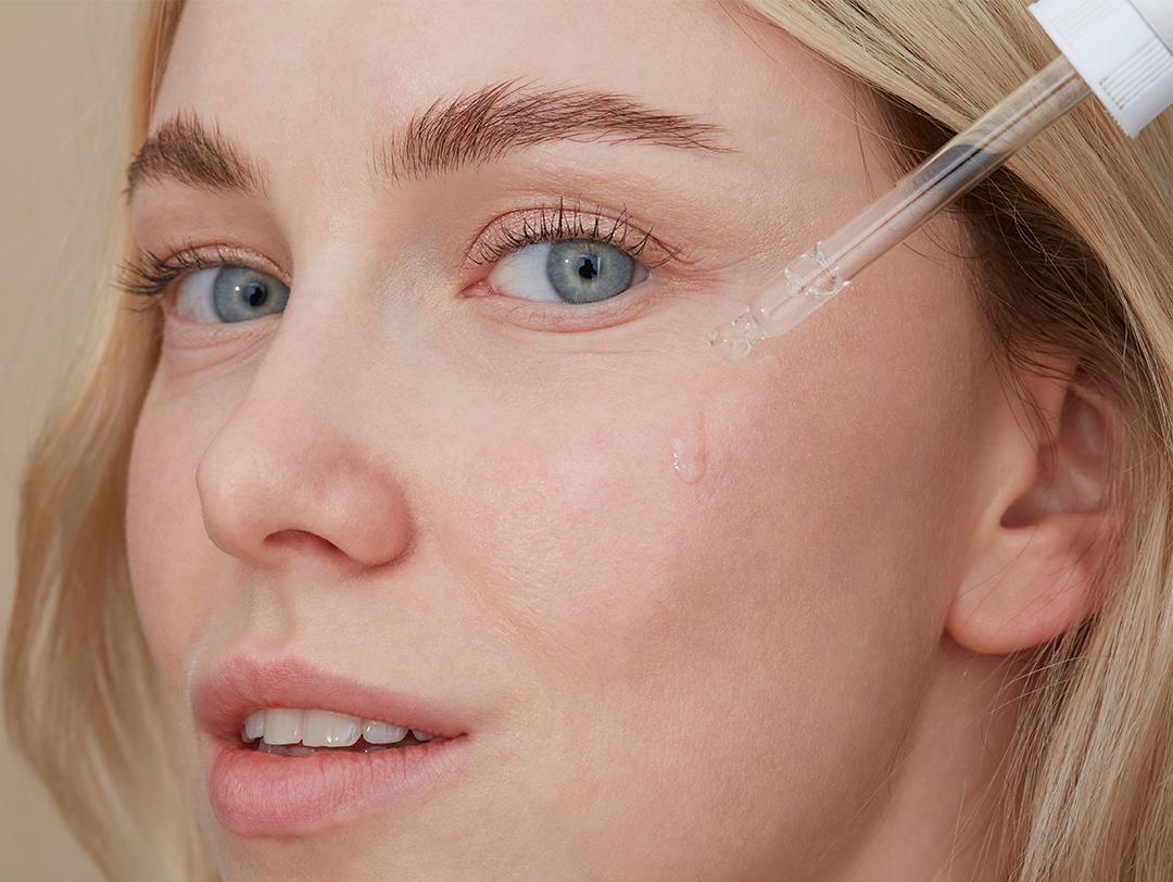 A photo of a woman with blonde hair applying serum on her face Desktop