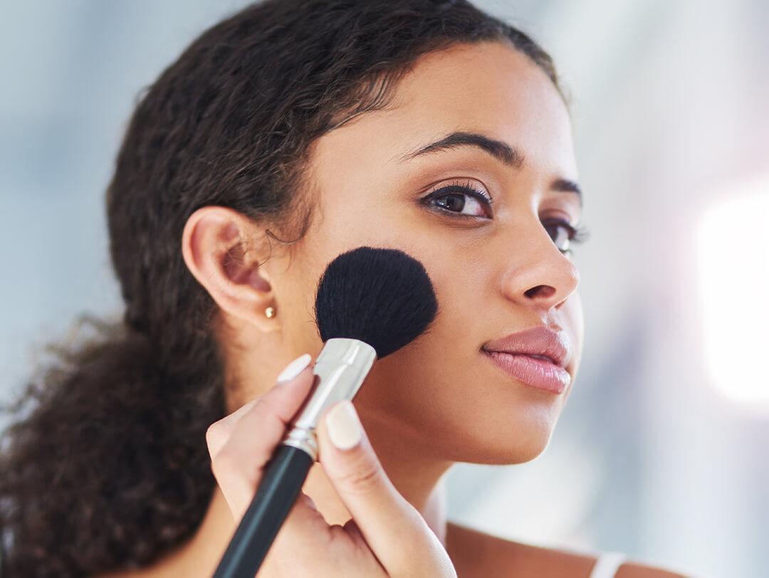 A photo of a young woman applying makeup to her cheeks using a black brush Desktop