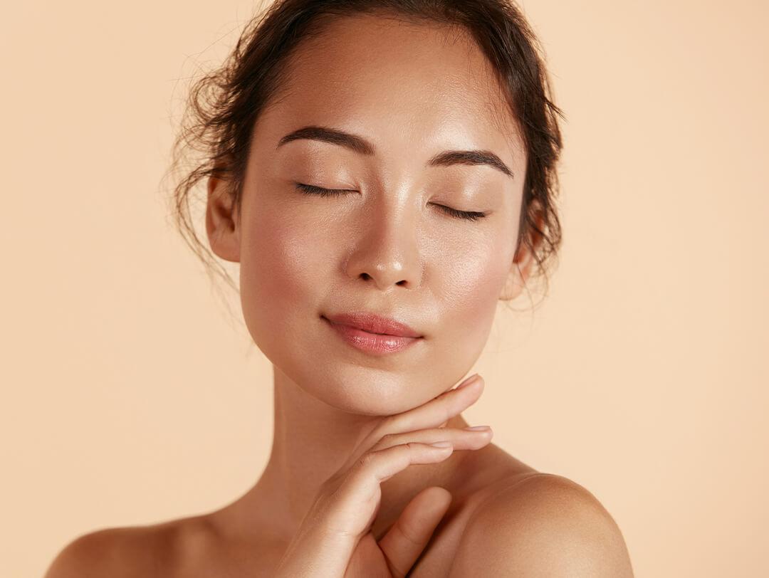 Beauty shot of a woman with clear skin posing with eyes closed against beige background Desktop