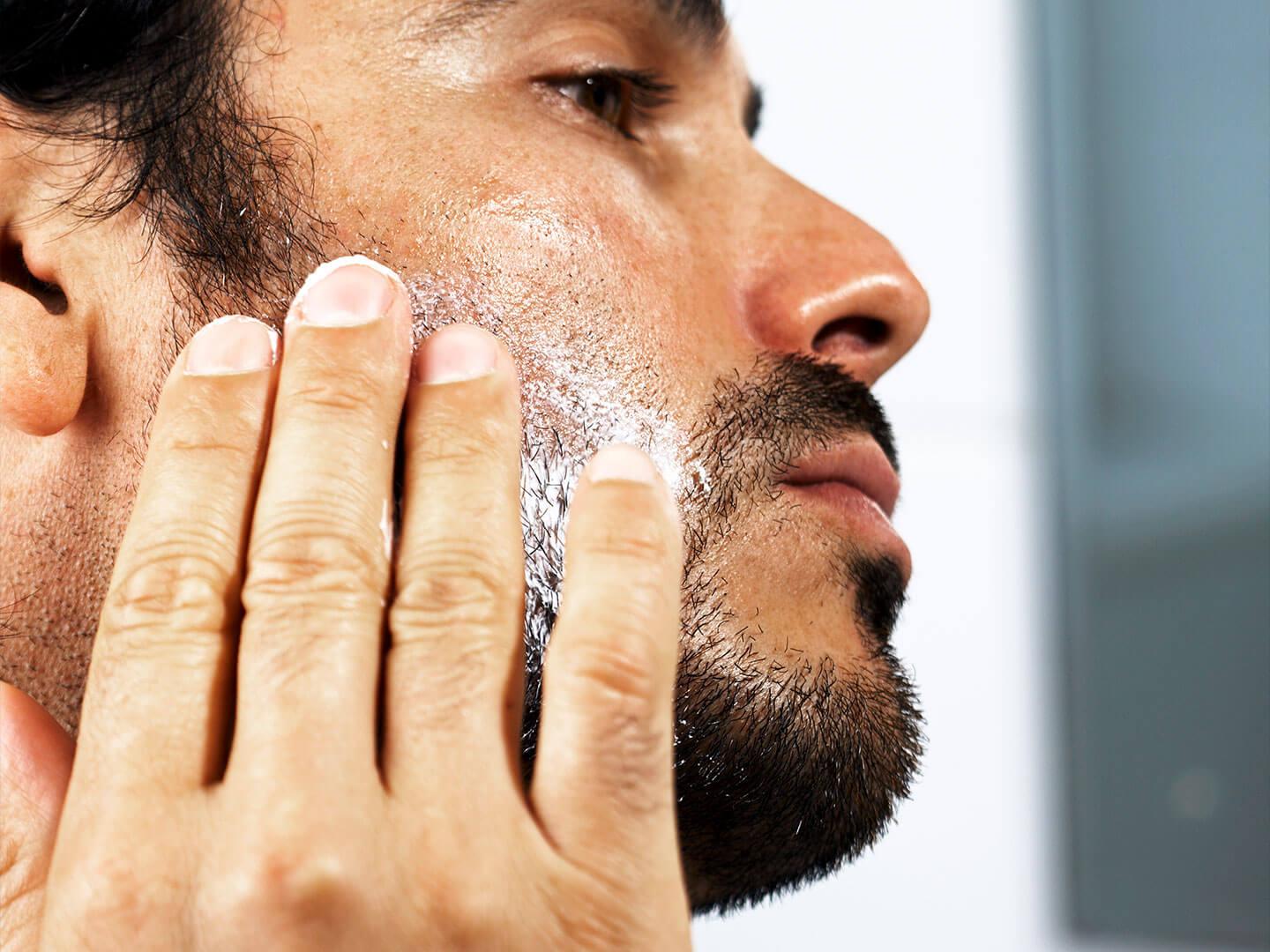 A detailed side profile of a man gently rubbing a cream into his slightly bearded skin Desktop