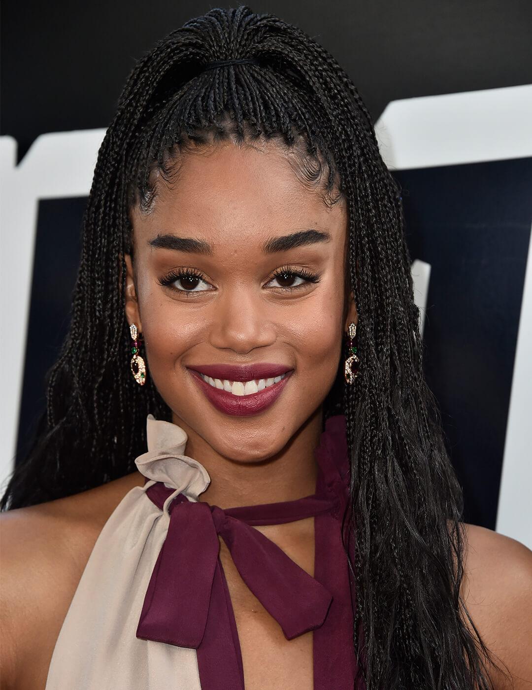 Laura Harrier in a maroon and cream dress and rocking a braided half updo hairstyle Mobile