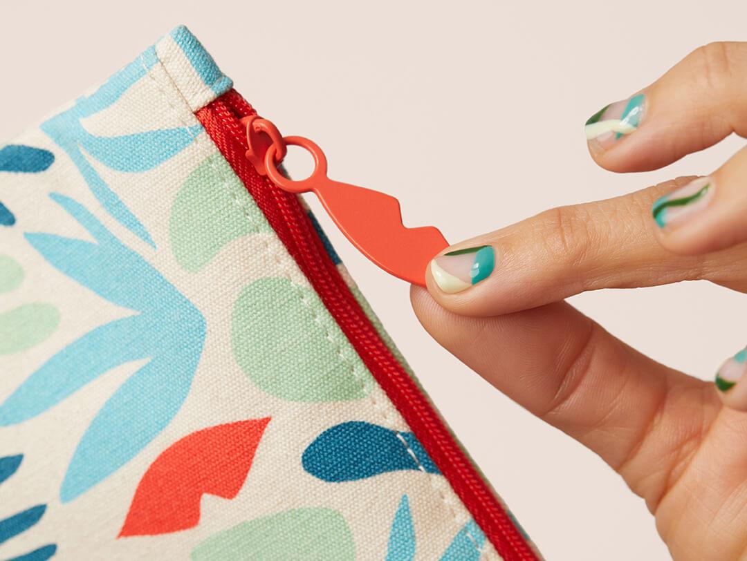 Close-up of fingers with colorful nail art holding the lips-shaped zipper of the April 2021 IPSY Glam Bag Desktop
