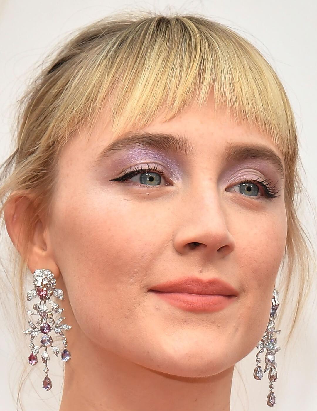 Saoirse Ronan rocking shimmery lavender eye makeup and silver dangling earrings on the red carpet Mobile
