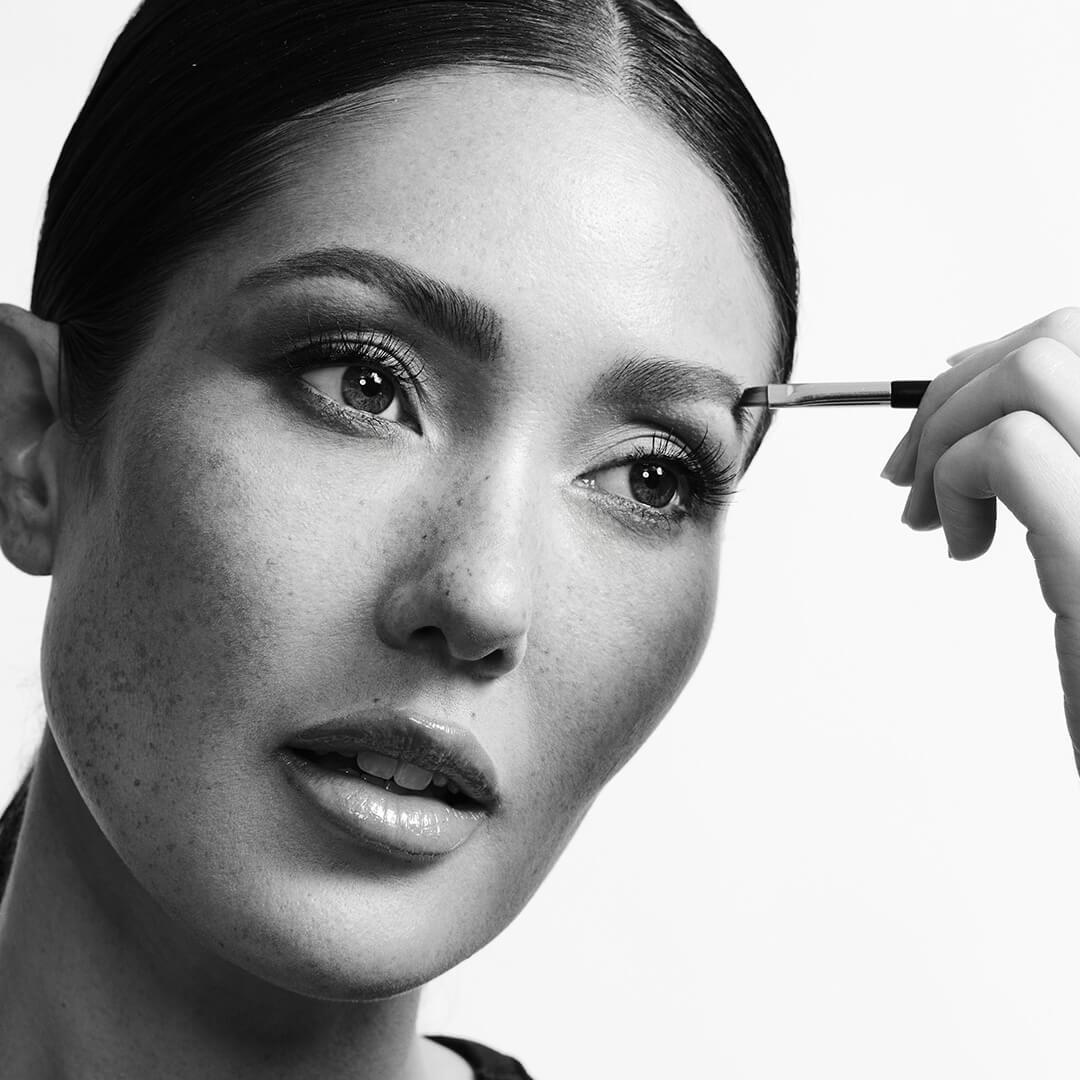 Black and white portrait of a beautiful model applying brow product with a brush Desktop