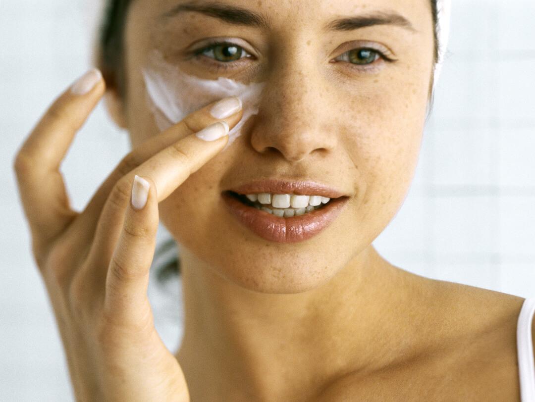 Close-up of a young woman putting cream under her eye Desktop