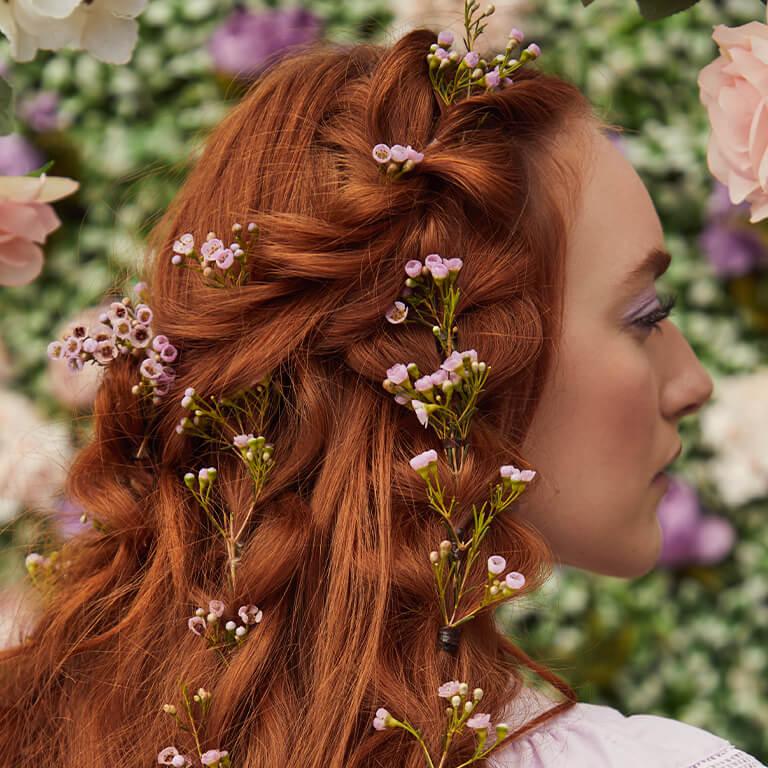 A close-up image of a model's braided red hair embellished with flowers Mobile