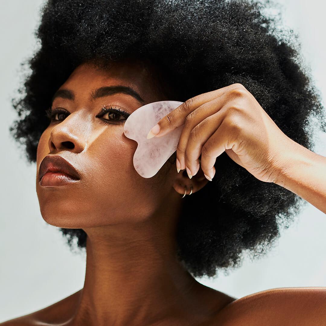 A photo of a woman using a gua sha on her face Mobile