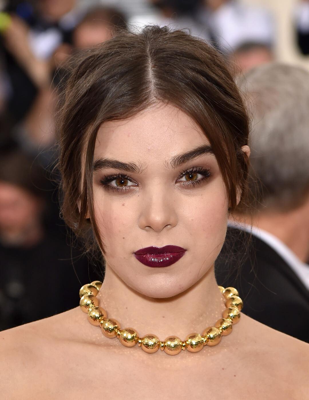Close-up of Hailee Steinfeld rocking a smoky eye makeup look, glossy burgundy lips, and golden big ball chain necklace Mobile