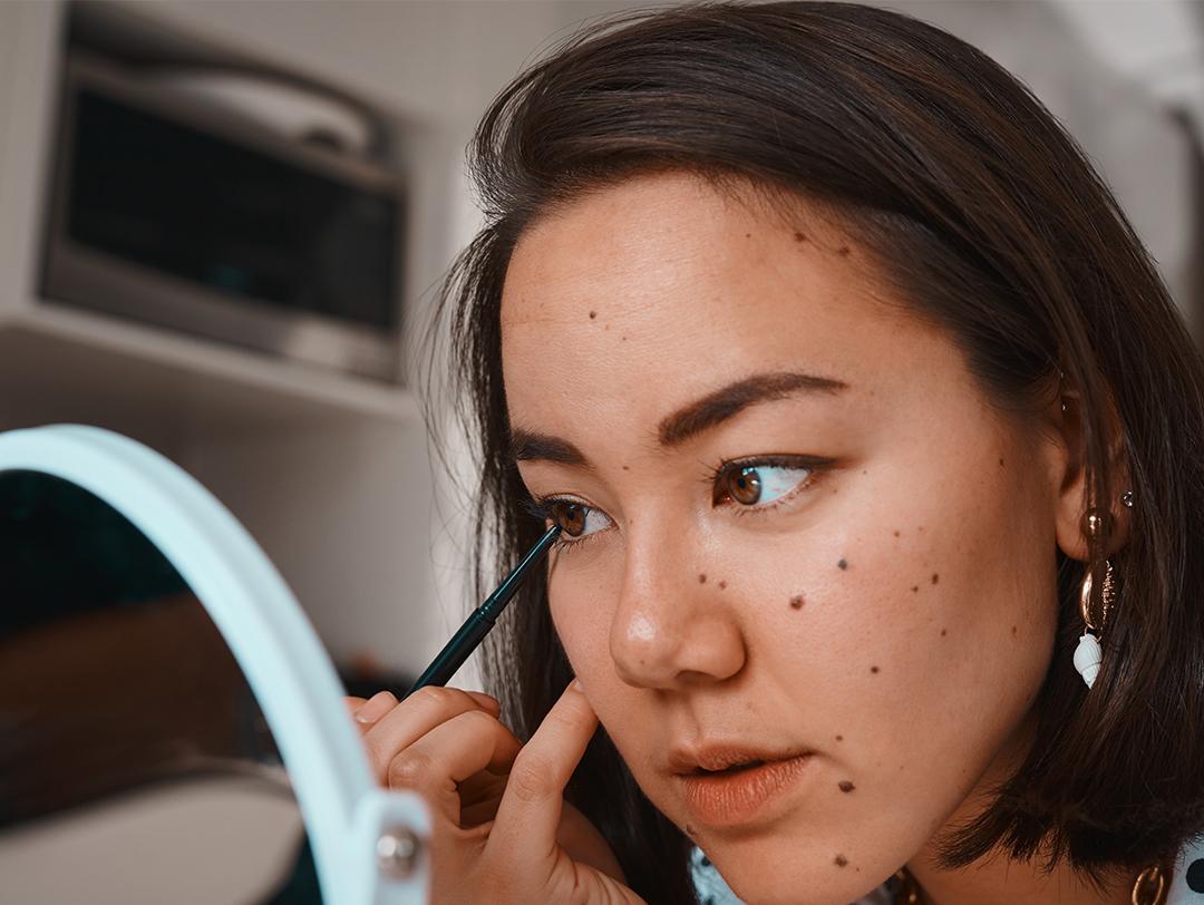 A photo of a young woman applying eyeliner in front of a mirror Desktop