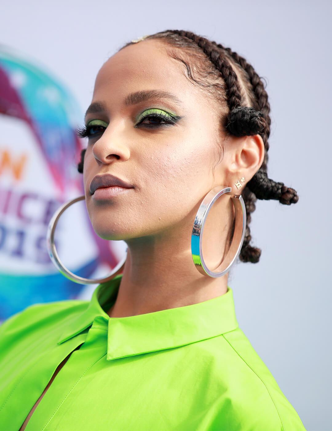 Megalyn Echikunwoke going bold in a neon green shirt, green eyeshadow look, big hoop earrings, and Bantu braids hairstyle Mobile