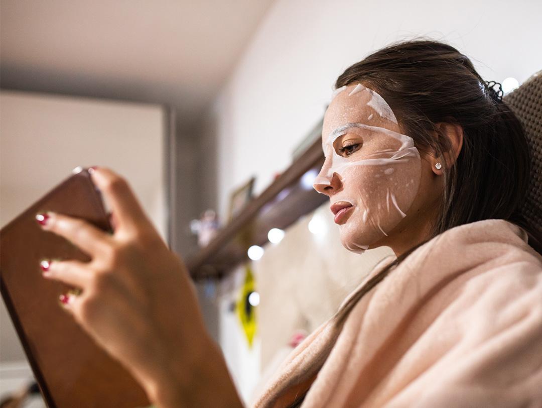 An image of a woman holding a book with a hydrating mask on her face Desktop