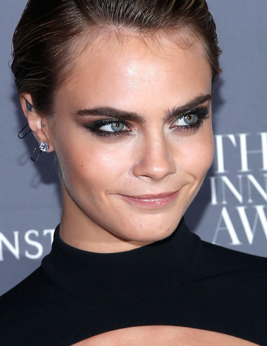 Cara Delevingne smirking and rocking a dark, metallic smoky eye makeup look Mobile