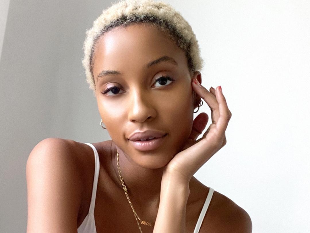 A photo of a model with blond dyed hair wearing a white tank top and gold necklace Desktop