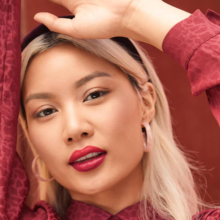 An image of a model wearing pink hoop earrings, red lipstick, and black headband is raising her hand Desktop