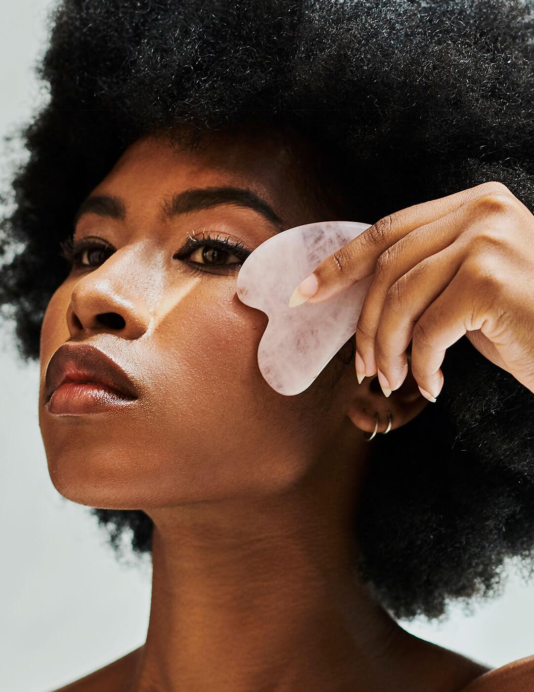 Beautiful young woman using gua sha quartz stone on her face for a skincare routine. Female using a beauty tool to firm, tighten and massage skin. Reducing wrinkles and promoting healthy cell renewal Desktop