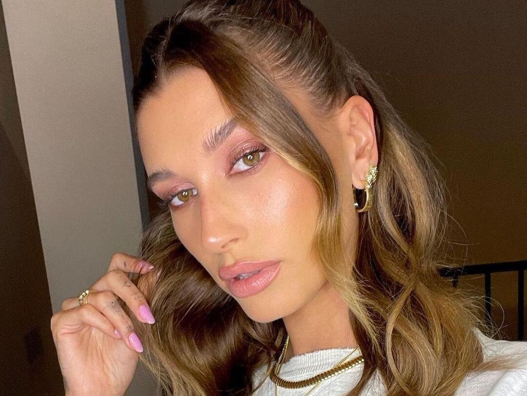 Selfie of Hailey Bieber rocking a half up ponytail hairstyle, pink monochromatic makeup look, and pink nail mani Desktop