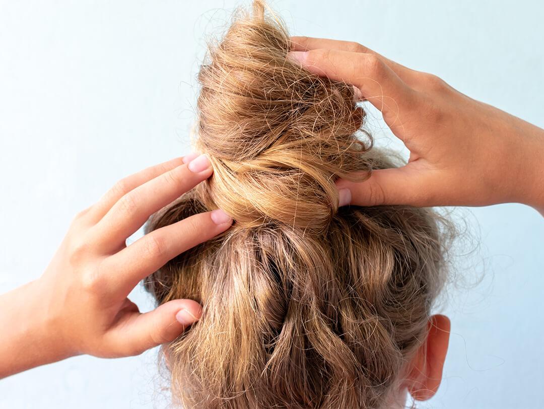 Close-up image of a woman styling her messy bun on light blue background Desktop