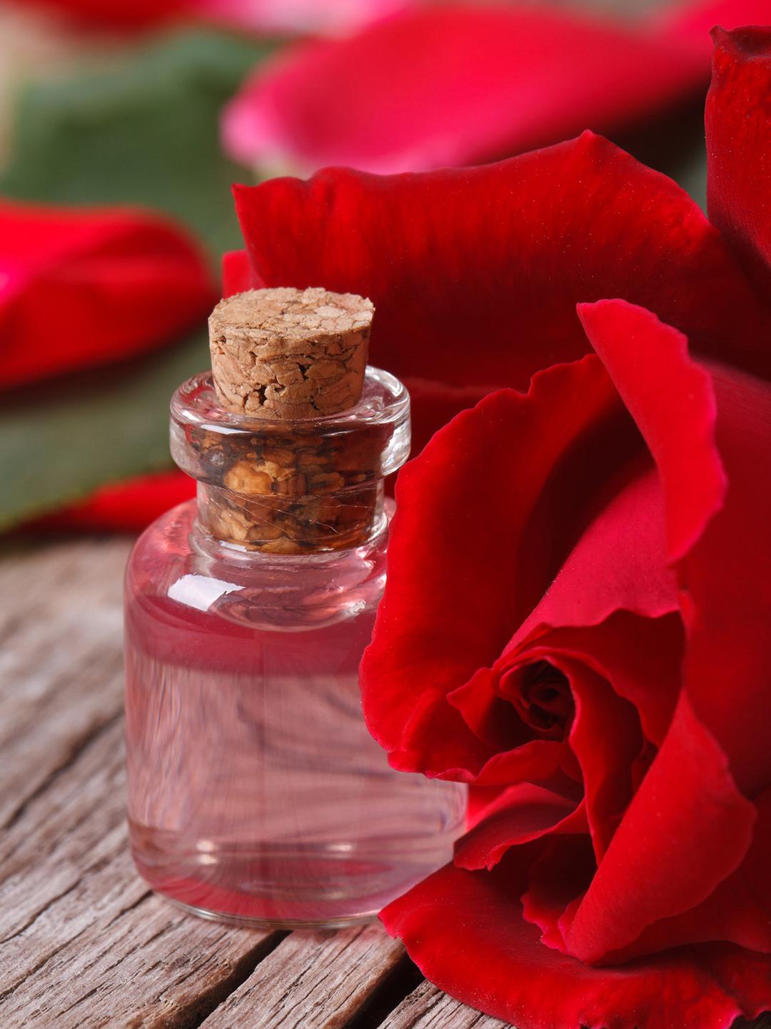 A close up look of a small clear bottle of rose water beside a red rose Desktop