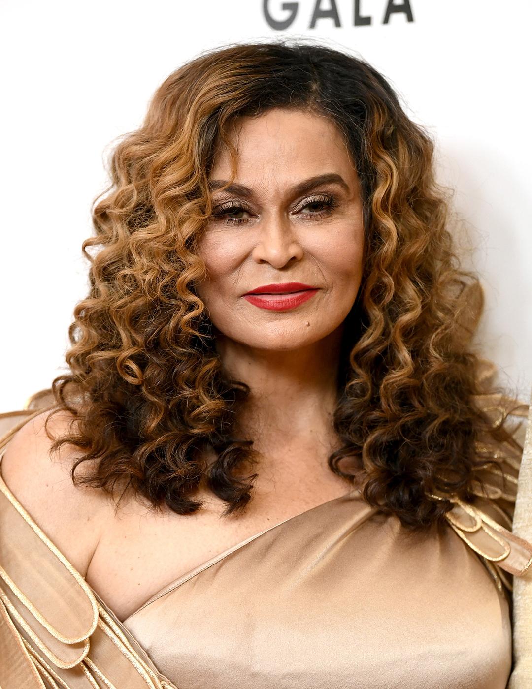 A photo of Tina Knowles in her honey-colored Mid-Length Coils dressed in a cream colored dress with a feather like cape Desktop