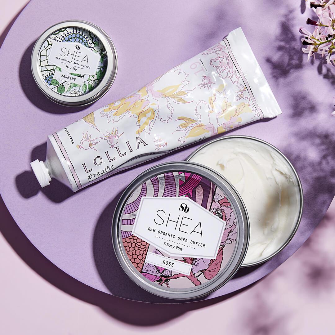 Flat lay image of SHEA BRAND Raw Organic Shea Butter in Jasmine, LOLLIA Breathe Shea Butter Handcreme, and SHEA BRAND Raw Organic Shea Butter in Rose and lavender background Desktop