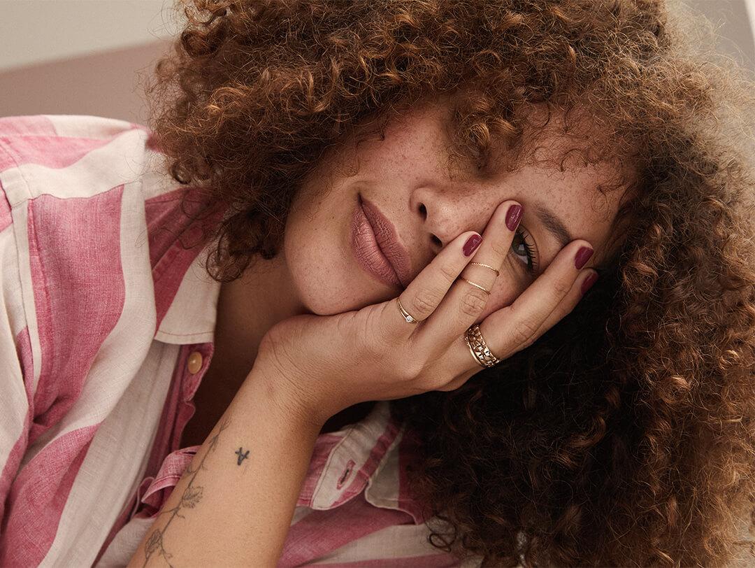 Close-up image of a curly-haired model posing while covering half of her face with her hand Desktop