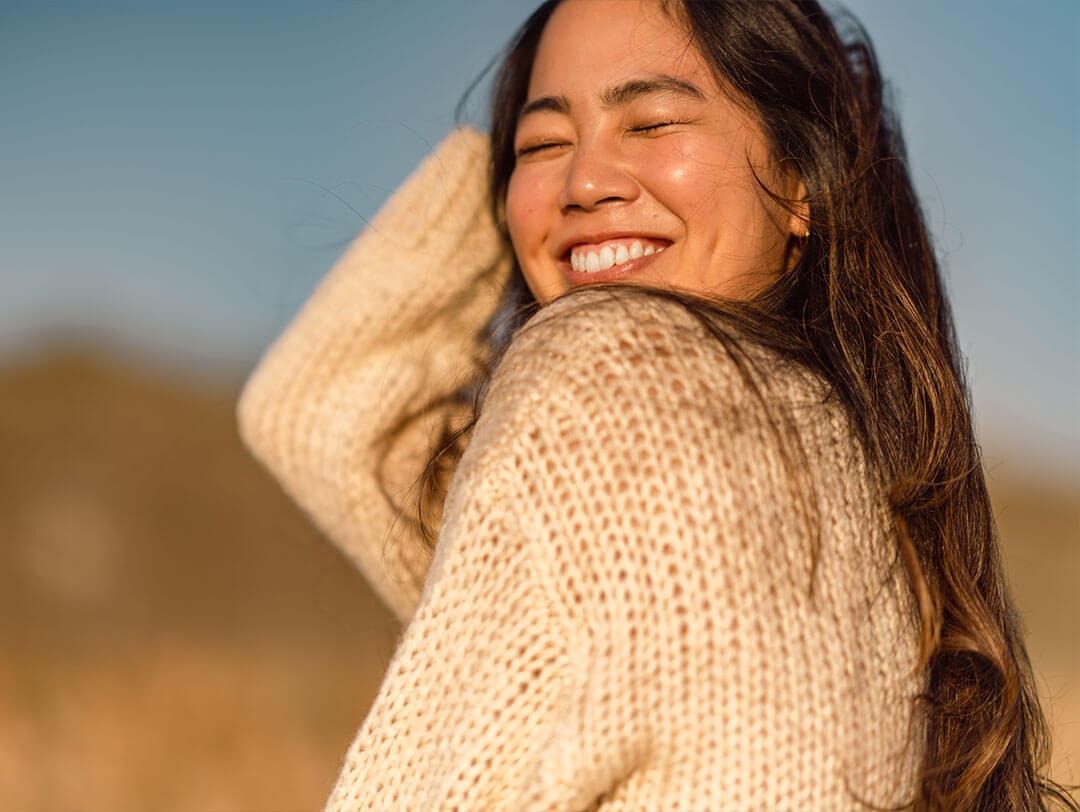 An image of a gorgeous woman with her hair gently tousled by the breeze, with her mesmerizing smile amidst the waning light of the day Desktop