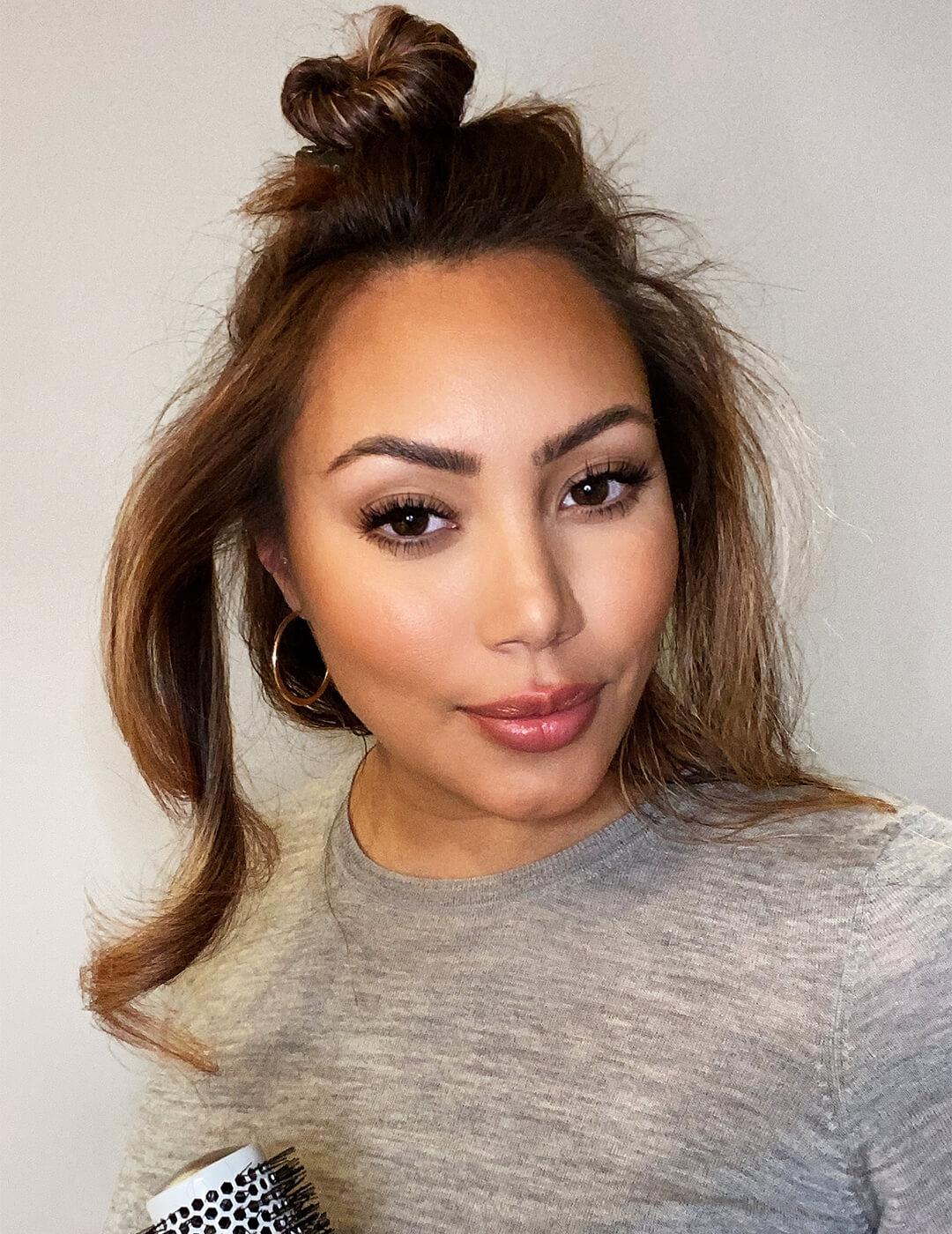 Close-up image of Cynthia Alvarez with her hair in a top knot and a loose section of wavy hair Mobile