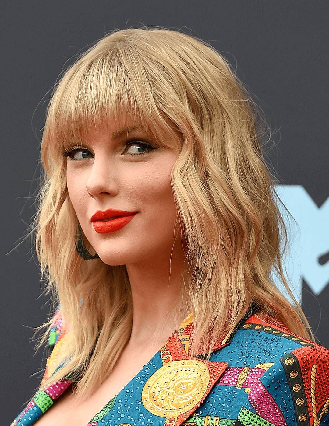 Taylor Swift sporting a modern shag hairstyle, bold red lips, and colorful suit Mobile