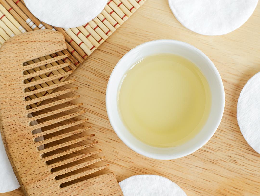 Flat lay image of a bowl of oil, wooden comb, and cotton pads on wooden surface Desktop