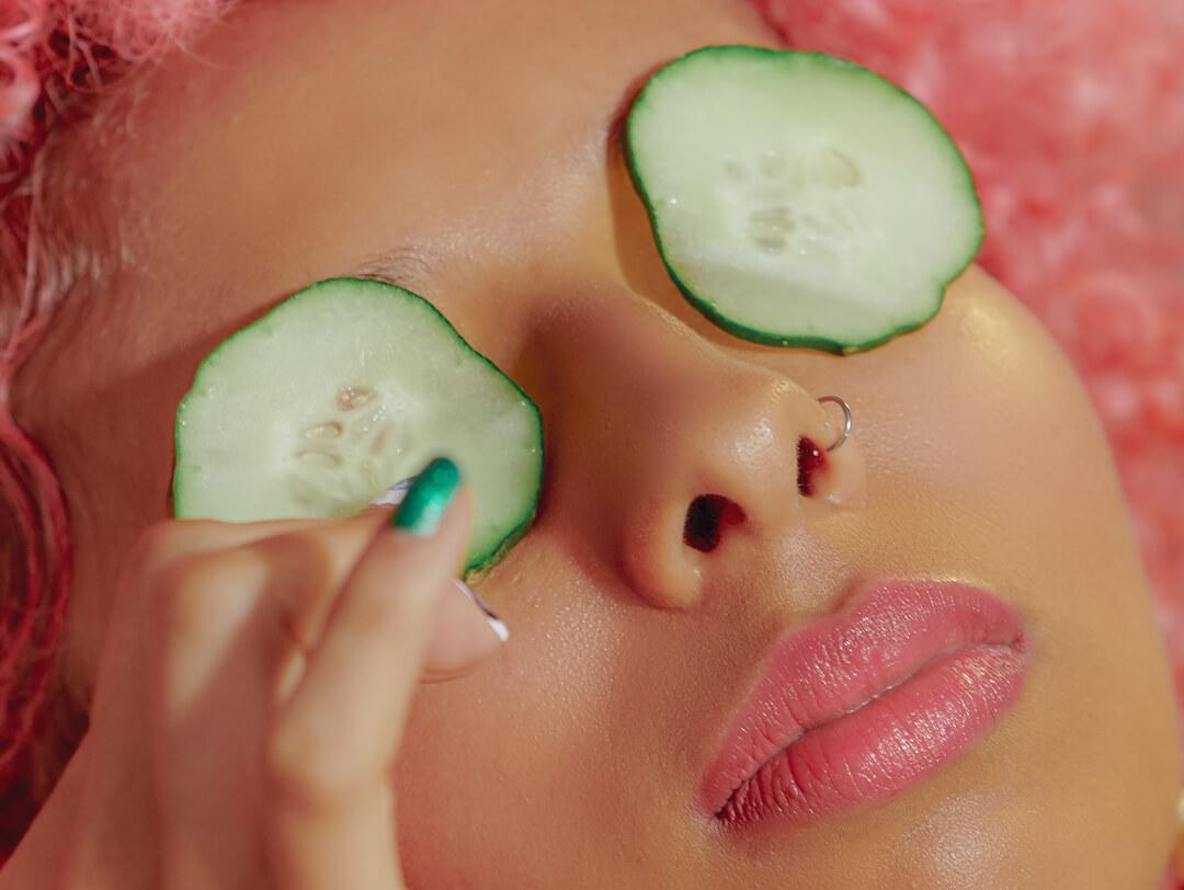 Young woman with pink hair putting on cucumber slices on her eyes Desktop