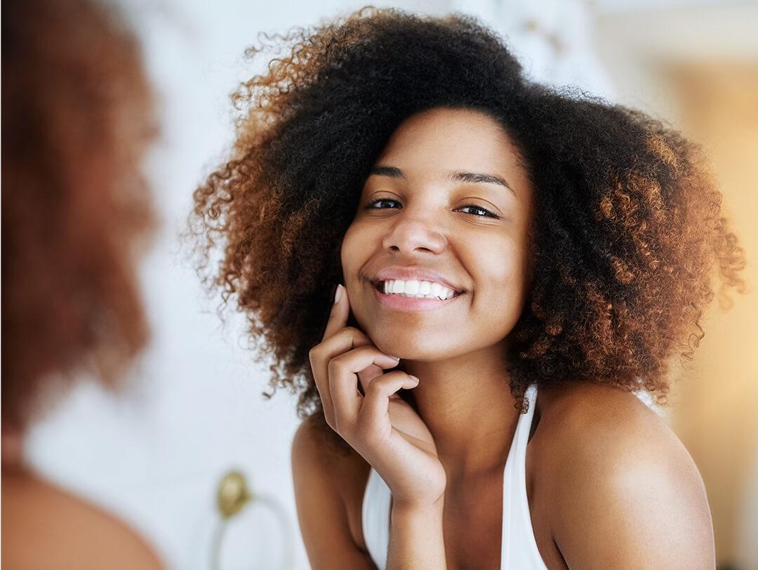 Smiling young woman checking her face in front of a mirror Desktop