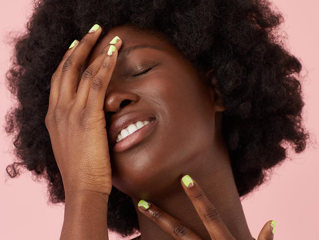 Close-up of a Black model with clear skin posing with her hands with lime green abstract nail art on pink background Desktop