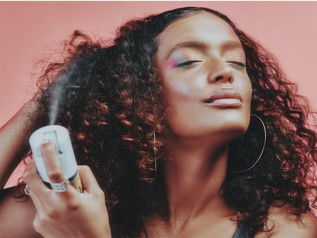 Close-up of a young woman with colorful eyeshadow look applying hairspray on her curly hair Desktop