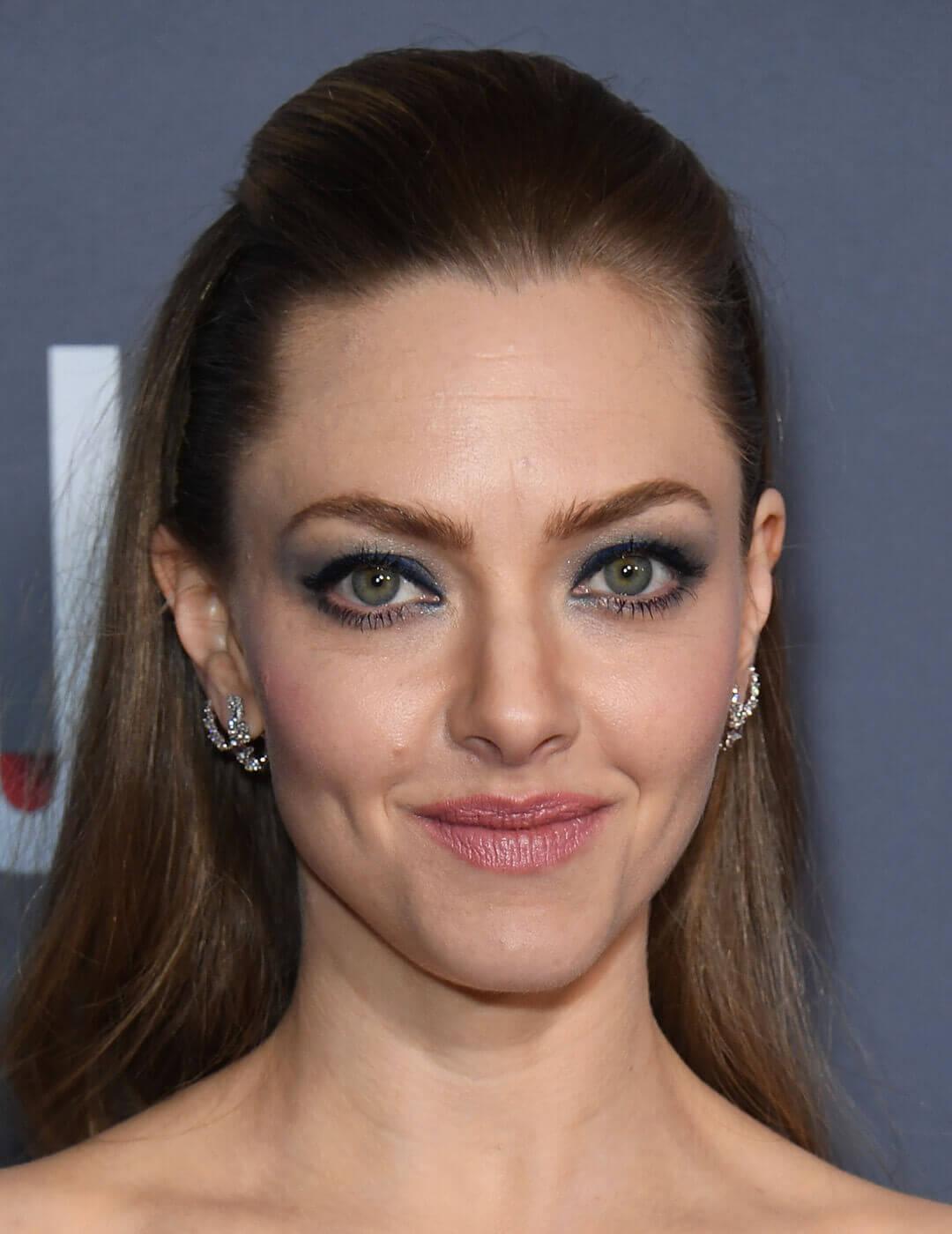 A close-up look of Amanda Seyfried showcasing her slicked-back blonde hairstyle and captivating round green eyes, adorned with a pair of diamond earrings Desktop