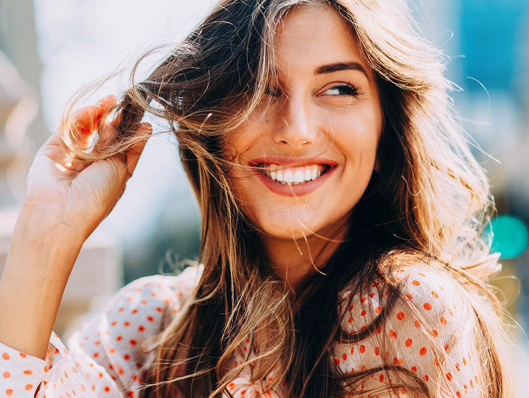 Portrait of a young woman smiling in the sun while holding her hair Desktop
