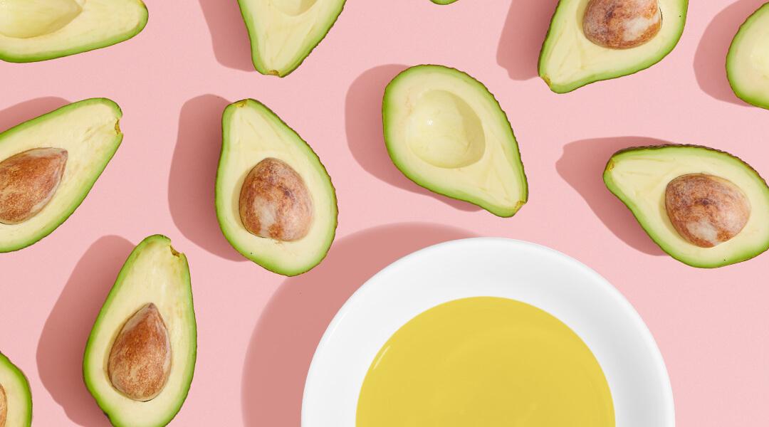 Image of avocado halves and a plate with yellow liquid on a pink surface Desktop