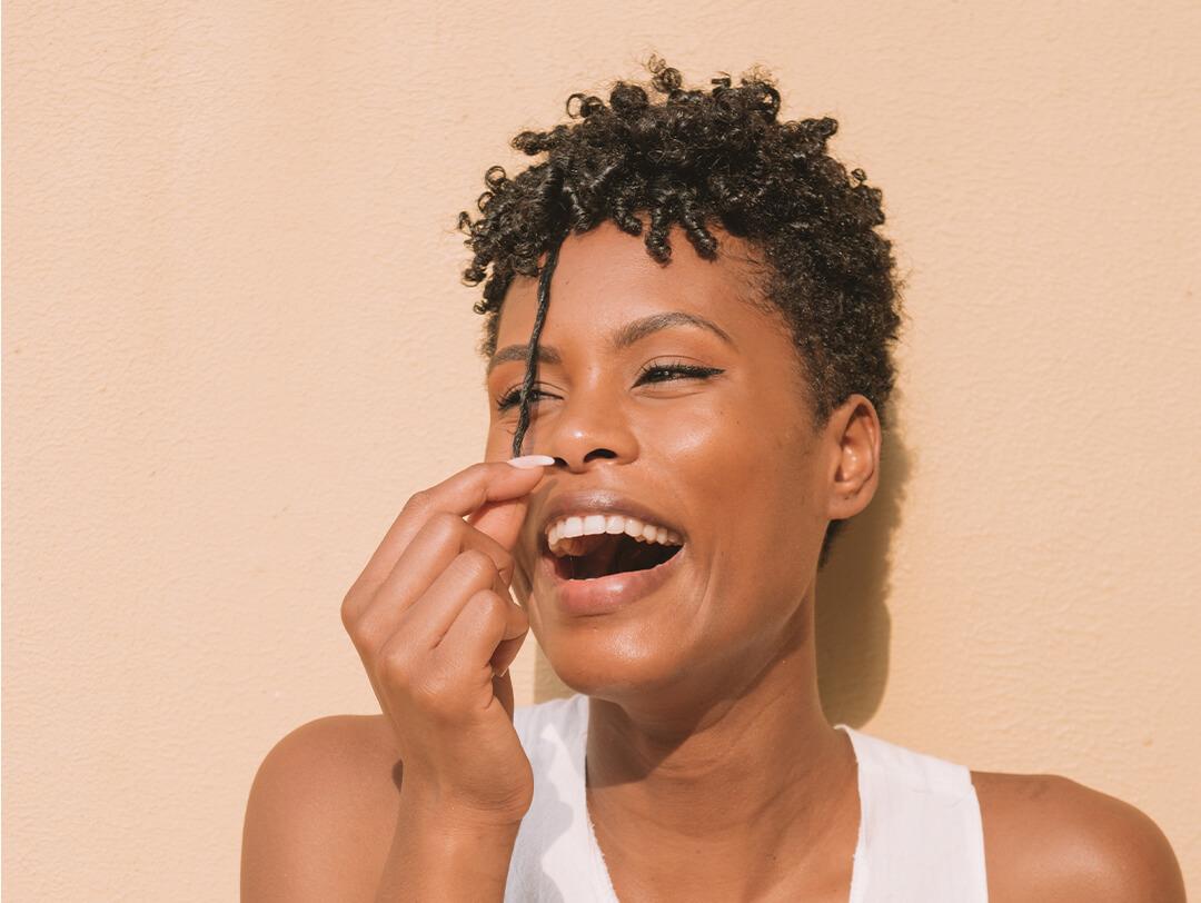 Image of a woman with tight curls pulling her hair while laughing Desktop