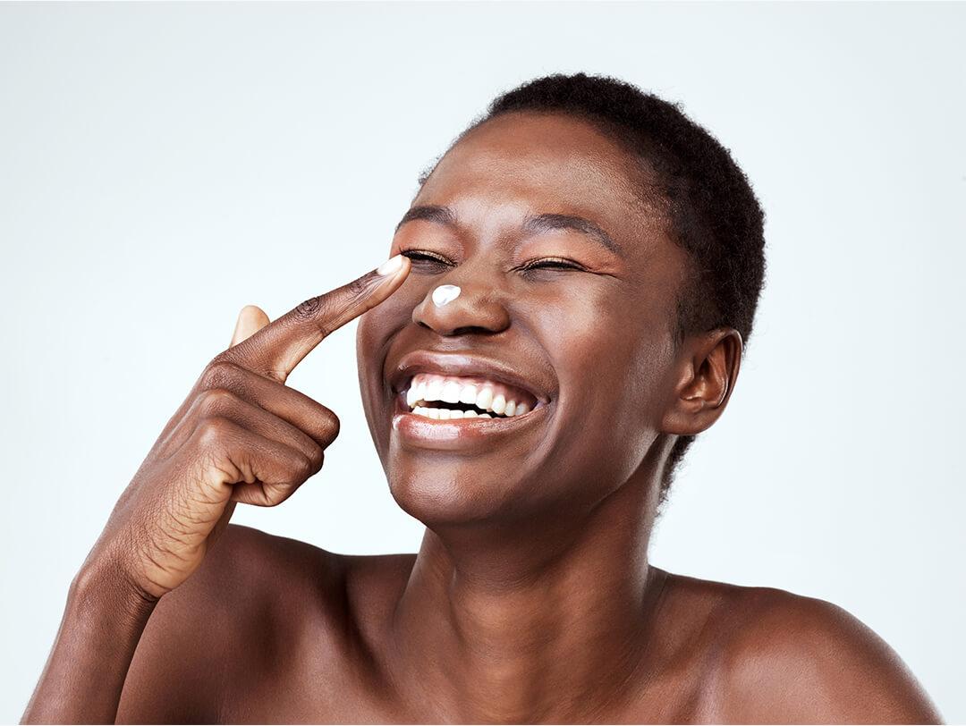 Close-up of a black American woman putting cream on her nose while laughing Desktop