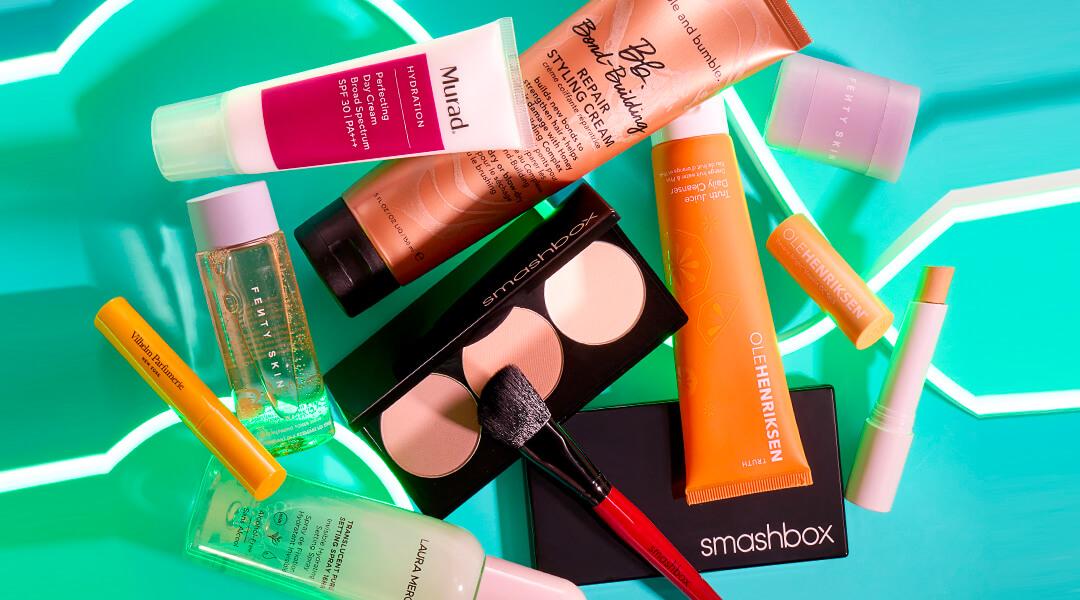 Skincare and makeup products from various brands scattered on blue background Desktop