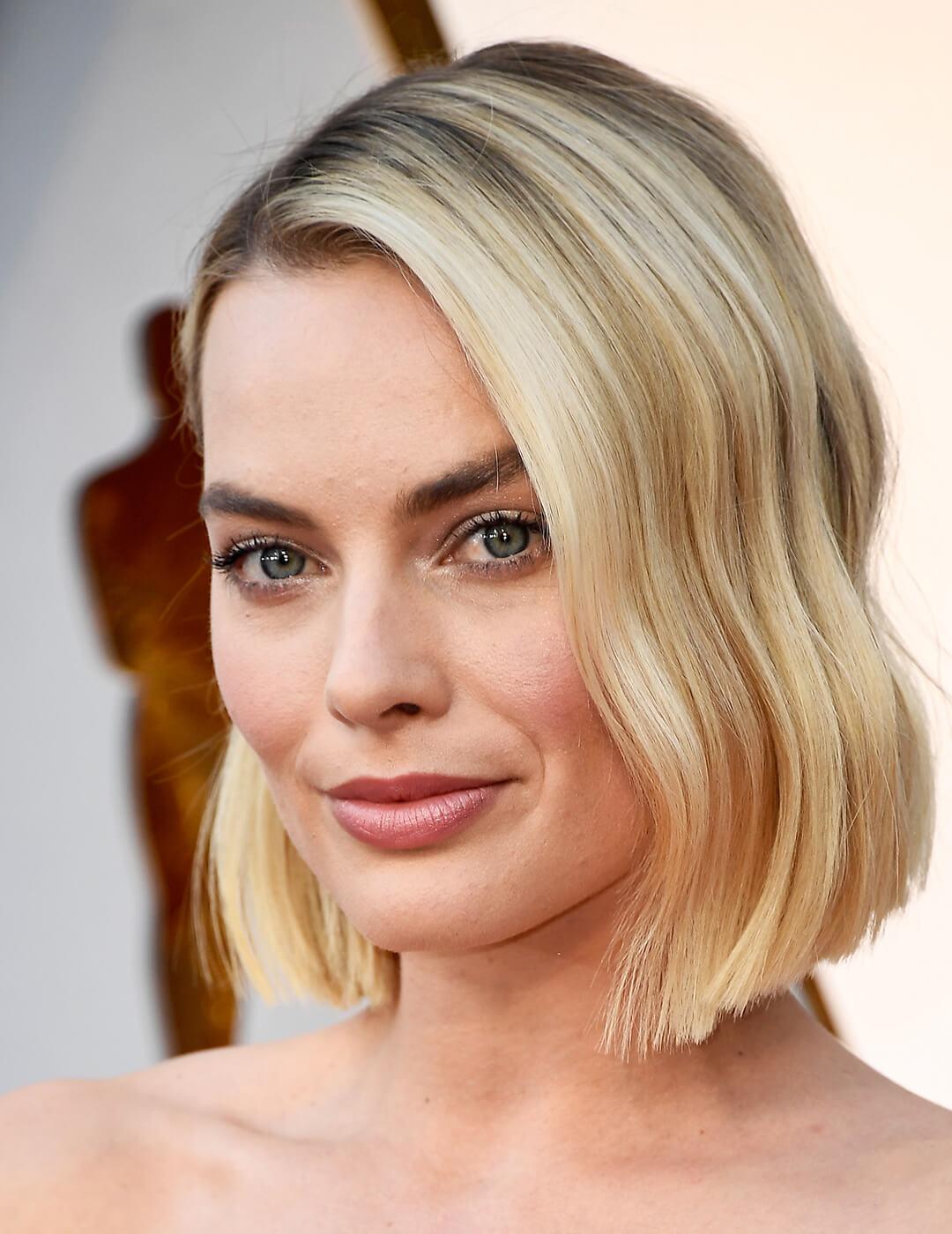 A photo of a green-eyed Margot Robbie smiling in the camera with her long bob hair style Mobile