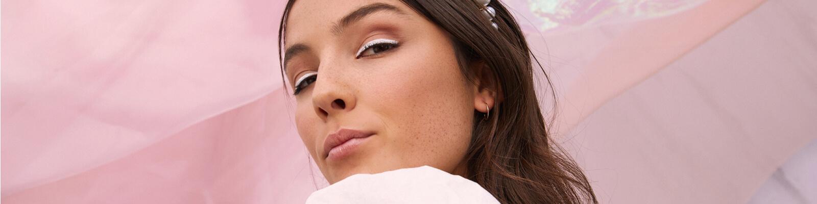 An image of a model wearing rose gold eyeshadow with white eyeliner and a pearl-studded headband Desktop
