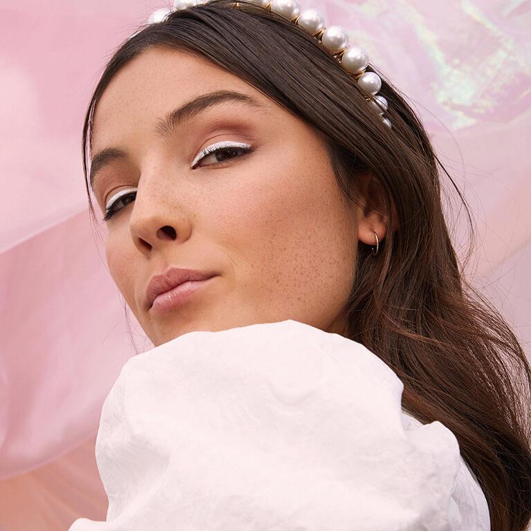 An image of a model wearing rose gold eyeshadow with white eyeliner and a pearl-studded headband Mobile